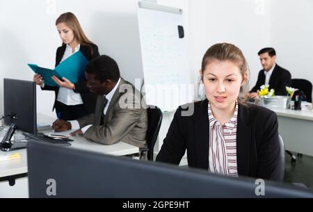 Young business woman working with laptop in workplace with international team Stock Photo