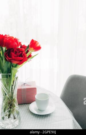 Red tulips bouquete on table, white coffee cup. Concept for greeting card for mothers day, international womans day or valentines day concept, birthda Stock Photo
