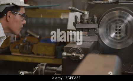 Asian professional mechanical engineer or operation man wearing uniform goggles safety working on workshop metal lathe industrial manufacturing factor Stock Photo