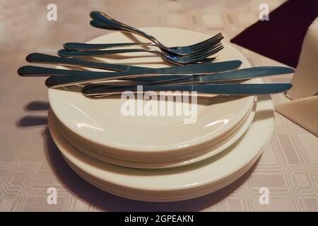 clean dishes are stacked with cutlery lying on top Stock Photo
