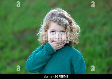 Surprised blond child with blue eyes covering his mouth Stock Photo