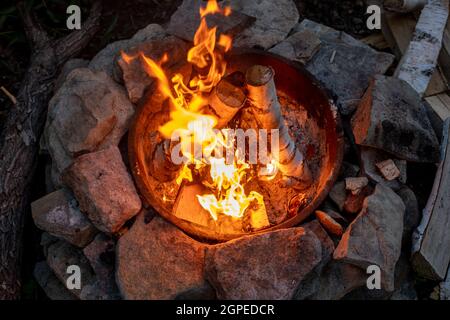 Birch logs burning in campfire surrounded by stones and other firewood Stock Photo