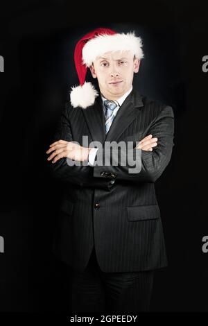 Christmas business. Xmas businessman in Santa hat standing with crossed arms on black background Stock Photo