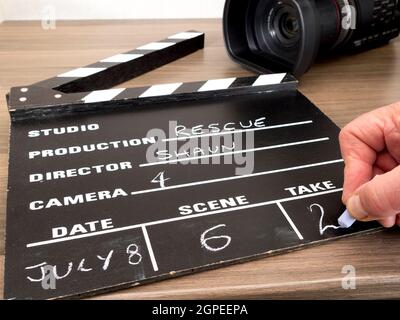 Closeup POV shot of a man's hand chalking Take 2 on a traditional clapper board, with a video camera behind. Stock Photo