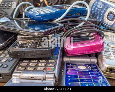 Closeup of a pile of old mobile phones and chargers – old technology ranging from the late 1990s up to the period before the advent of smartphones. Stock Photo