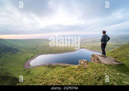 Man overlooking Llyn y Fan Fach lake. Brecon Beacons National Park. Black Mountain, Carmarthenshire, South Wales, the United Kingdom. Hiking in the UK concept. Stock Photo