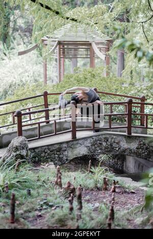 Sports girl doing stretching with her leg lifted on the railing of the bridge in park Stock Photo