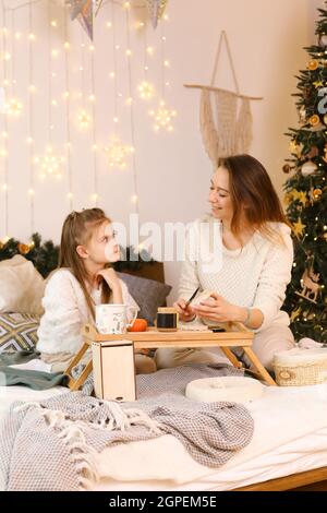 Mother and daughter preparing breakfast. They smear almond cashew or peanut butter on bread. Stock Photo