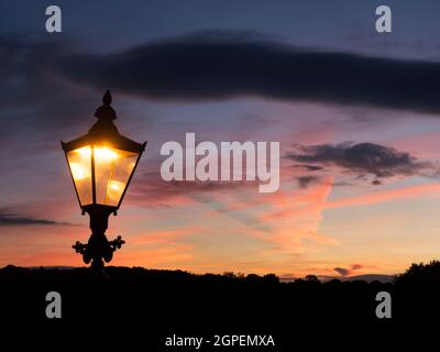 Ornate street lamp silhouetted against a sunset sky on the autumn equinox in the Castle Grounds at Knaresborough North Yorkshire England Stock Photo