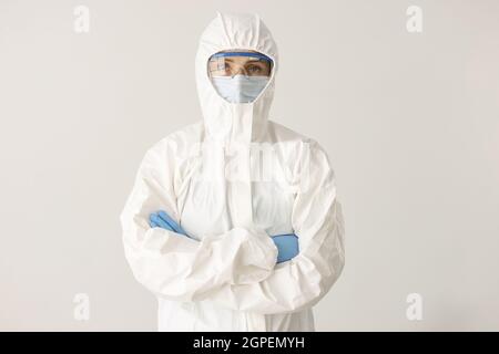 Woman doctor or scientist stands in protective suit, mask and glasses with folded arms on white background Stock Photo