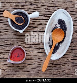 Black sesame oil and sesame seeds in white bowl set up on grunge wooden background. Stock Photo