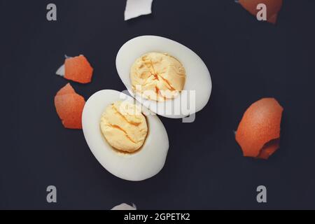 The halves of a peeled boiled egg lie on a dark background next to a brown broken shell. Healthy food. Stock Photo