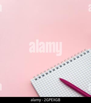 A blank checkered sheet of paper. Notepad and pen on pink. Pink Pen. Notepad spring Spiral spiral checked sheets. Vertically. Stock Photo