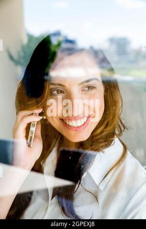 Successful young business woman reflects in her office window as she talks on a mobile phone Stock Photo