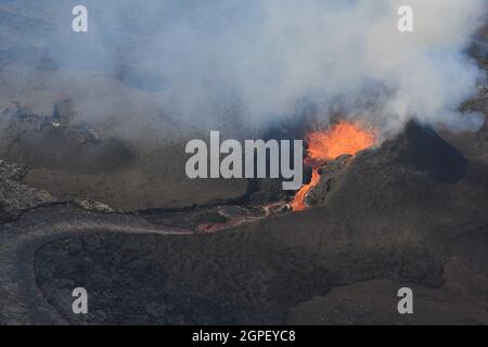 Erupting vent and lava flow at Fagradalsfjall, Iceland. The lava field is black, with red and orange molten lava. Volcanic gas rises from teh crater. Stock Photo