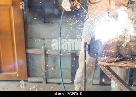 Sparks fly as a full-helmeted welder spot-welds a metal rod Stock Photo