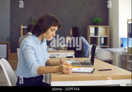 Busy woman sitting at a table and checking documents while working in a modern coworking center. Stock Photo