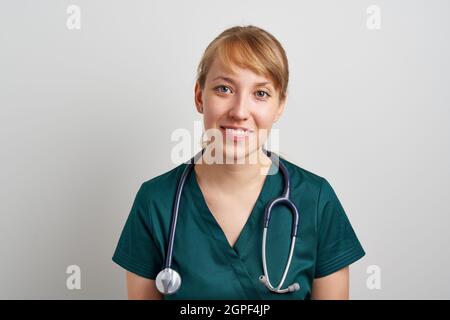 Smiling young female nursing assistant with phonendoscope in green uniform. Surgeon emergency Stock Photo