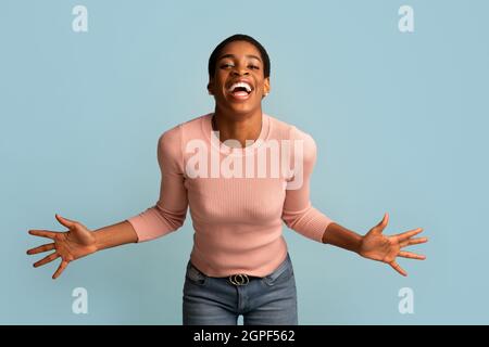 Surprise. Cheerful Black Lady Spreading Hands And Laughing At Camera Stock Photo