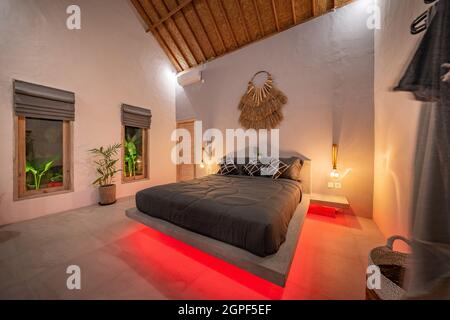 modern stone pine bed with red led lighting, wall lamps. Bedroom in luxury loft apartment - shot in low light to highlight the atmosphere of red led Stock Photo