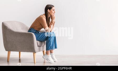 Thoughtful young woman looking at empty space with pensive dreamy expression against white studio wall, banner design Stock Photo