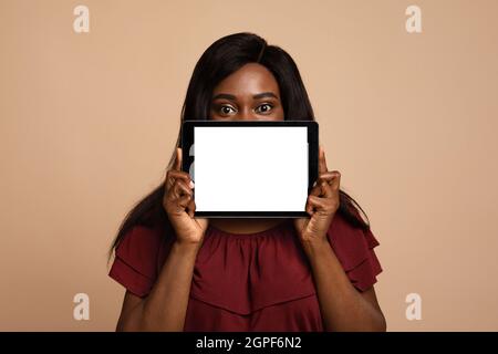 Long-haired black woman hiding behind digital tablet with empty screen Stock Photo