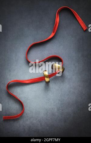 Two rings and a red ribbon on dark textured background Stock Photo