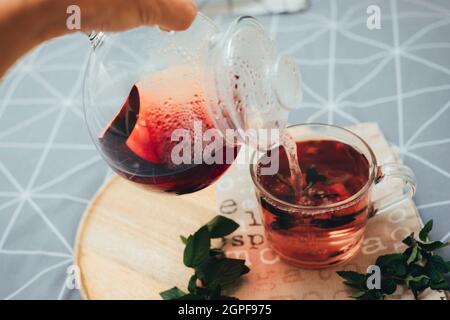 Herbal tea is poured from a teapot into a cup on a wooden tray on the bed. Cozy autumn. Breakfast in bedroom. Top view. Stock Photo