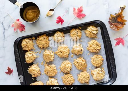 Top down view of a baking sheet of maple cookies drizzled with maple syrup, with maple leaves scattered around. Stock Photo