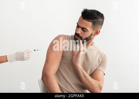 Young Arab guy stopping medical worker from making covid vaccine shot, being afraid of coronavirus immunization Stock Photo