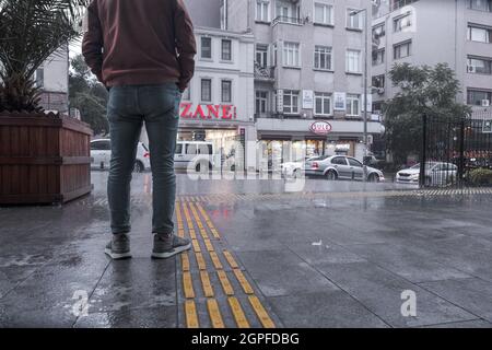 Beyoglu, Istanbul, Turkey - 06.18.2021: low angle view of a Turkish man standing near rainy street while raining heavily outside and rain drops all ar Stock Photo