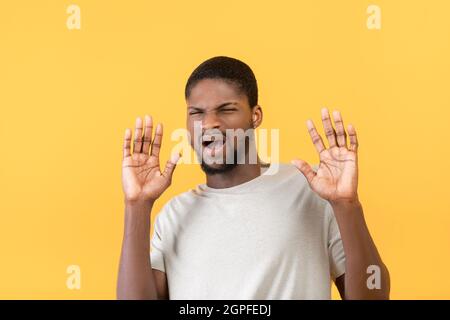 Oh no. Disgusted black man showing refuse gesture with hands, keeping away of something, yellow background Stock Photo