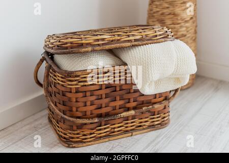 A wicker straw and bamboo chest of drawers, in the interior with bedspreads, blankets, a blanket and towels. For interior decoration. Stock Photo