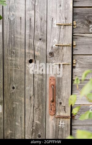 Door of an old wooden toilet or barn with a rusty doorknob and three latches, in a countryside. Stock Photo