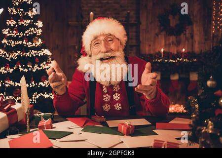 Photo of funny friendly santa claus sit workspace webcamera communication wear hat sweater in north pole office indoors Stock Photo