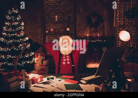 Photo of relaxed santa claus sit comfortable workspace enjoy break wear hat pullover in north pole office indoors Stock Photo