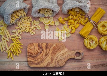 Italian foods concept and menu design . Various kind of Pasta Elbow Macaroni ,Farfalle ,Rigatoni ,gnocco Sardo in hemp sack bags set up on brown woode Stock Photo