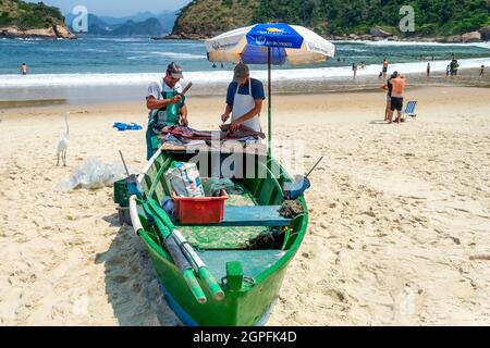 Brazilian fishermen preparing freshly caught fish in a boat in the Piratininga beach in Niteroi, Rio de Janeiro, Brazil. The practice of artisanal fis Stock Photo