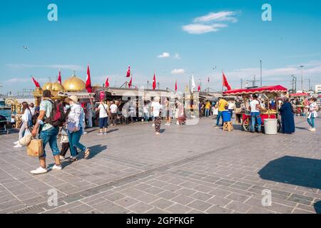 Eminonu, Istanbul, Turkey - 07.05.2021: a lot of Turkish people and tourists with mask walking around Eminonu square with boat restaurants selling fis Stock Photo