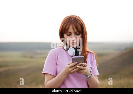 Young redhead woman with white headphones looks in the smartphone Stock Photo