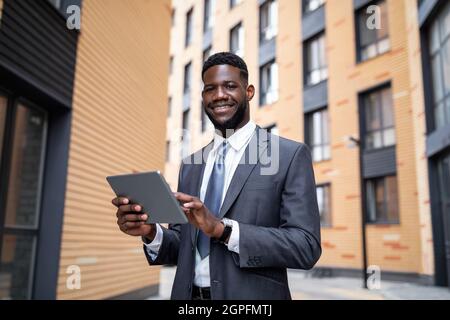Happy african american company employee working with tablet computer during lunch break outdoors, free space Stock Photo