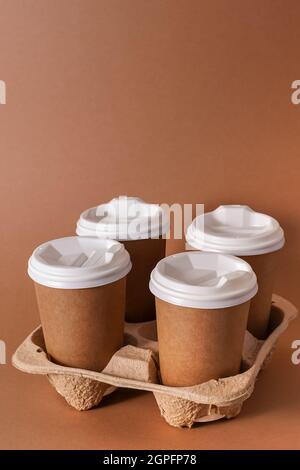 Paper cups in a cup holder for takeaway coffee. Paper cup with a drink. Disposable tableware. Eco cardboard recyclable. Brown background. Copy space. Breakfast delivery to the office. Stock Photo
