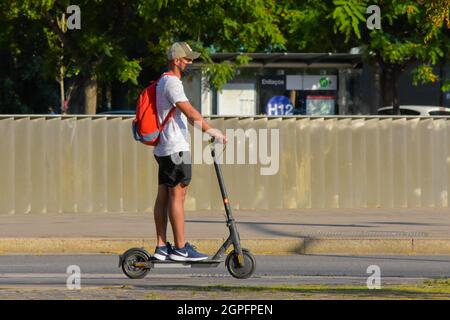 Young man riding on electric scooter in a street. Barcelona, Catalonia, Spain. Stock Photo