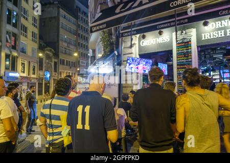Beyoglu, Istanbul, Turkey - 07.07.2021: several foreign tourists and Turkish people watch world cup football matches together in a bar outside at nigh Stock Photo
