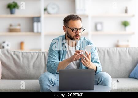 Serious young freelancer using laptop and smartphone at home office Stock Photo