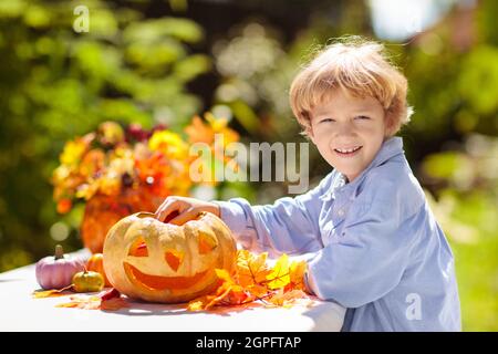 Family carving pumpkin for Halloween celebration. Boy cutting jack o lantern for traditional trick or treat decoration in sunny garden. Kid decorating Stock Photo