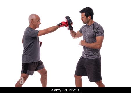 Elderly man hits with boxing glove in defense, personal fitness trainer, concept of working together. On white background. Stock Photo