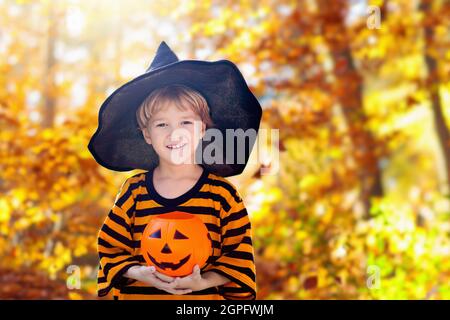 Kids trick or treat in Halloween costume. Children in colorful dress up with candy bucket on suburban street. Little boy and girl trick or treating Stock Photo