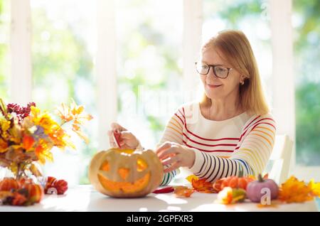 Family carving pumpkin for Halloween celebration. Woman cutting jack o lantern for traditional trick or treat decoration. Female decorate home. Stock Photo