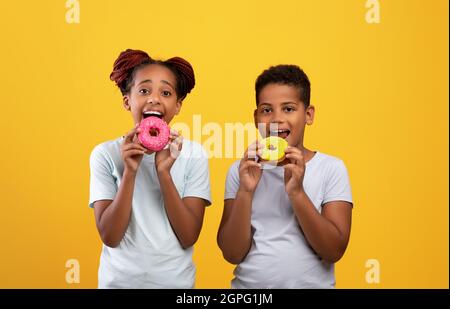 Happy black boy and girl eating delicious donuts Stock Photo